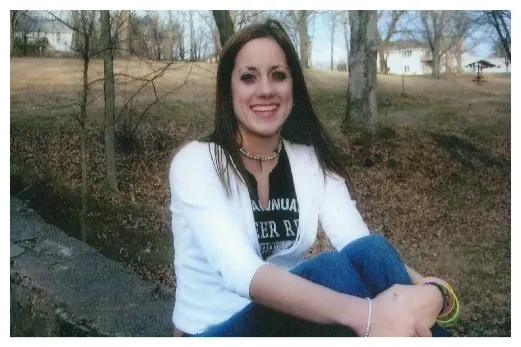 A woman sitting on the ground in front of trees.