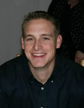 A man smiling for the camera in front of a wall.