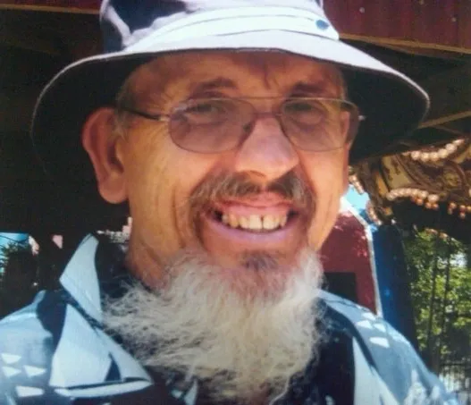 A man with long beard and hat smiling for the camera.