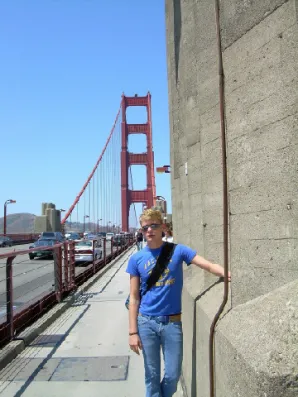 A man standing on the side of a road near a bridge.