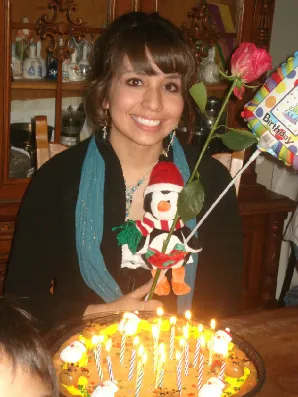 A woman holding a penguin and rose in front of a cake.