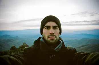 A man in black jacket and hat on top of hill.