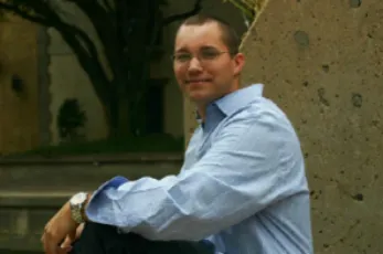 A man in blue shirt and glasses sitting on the ground.