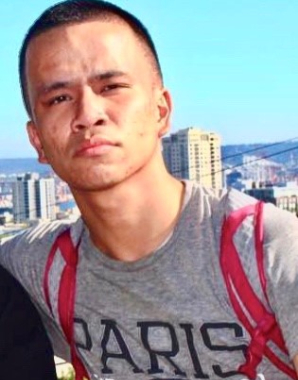 A man with short hair and a gray shirt is standing in front of the city.