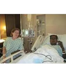 A woman sitting next to a man in a hospital bed.