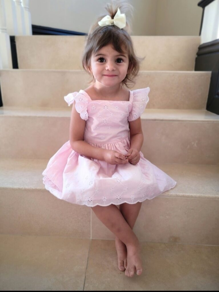 A little girl in pink dress sitting on steps.