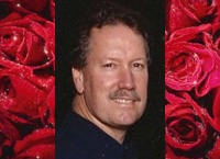 A man with a beard and mustache in front of red roses.