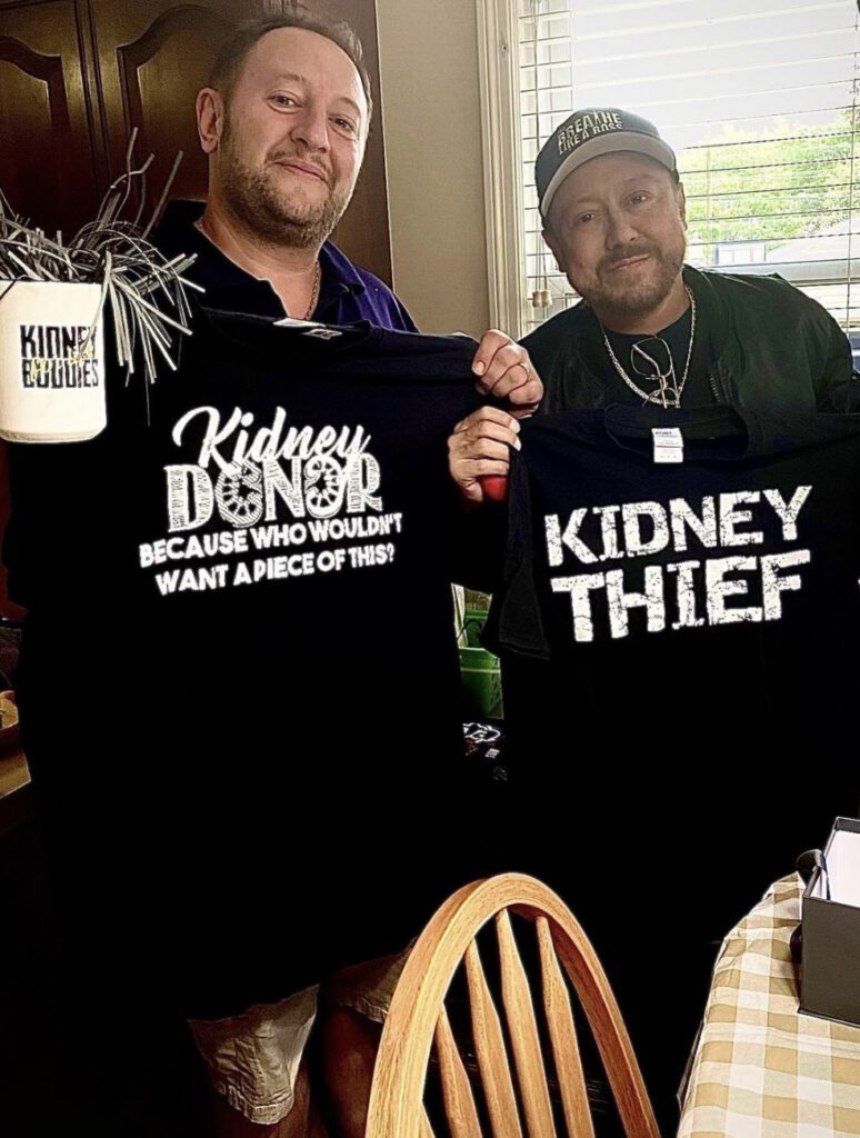 Two men holding up black shirts with the words kidney denial and kidney thief on them.