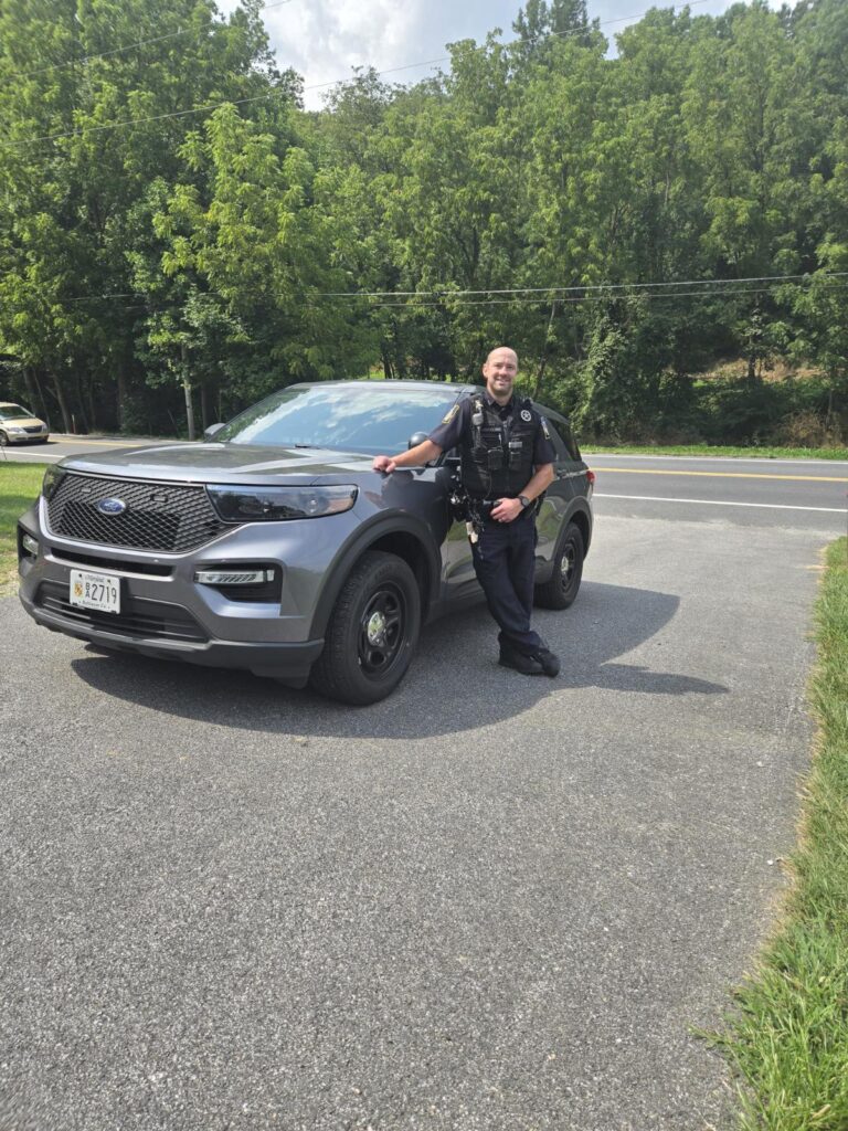 Police officer standing next to a police SUV on a sunny day.