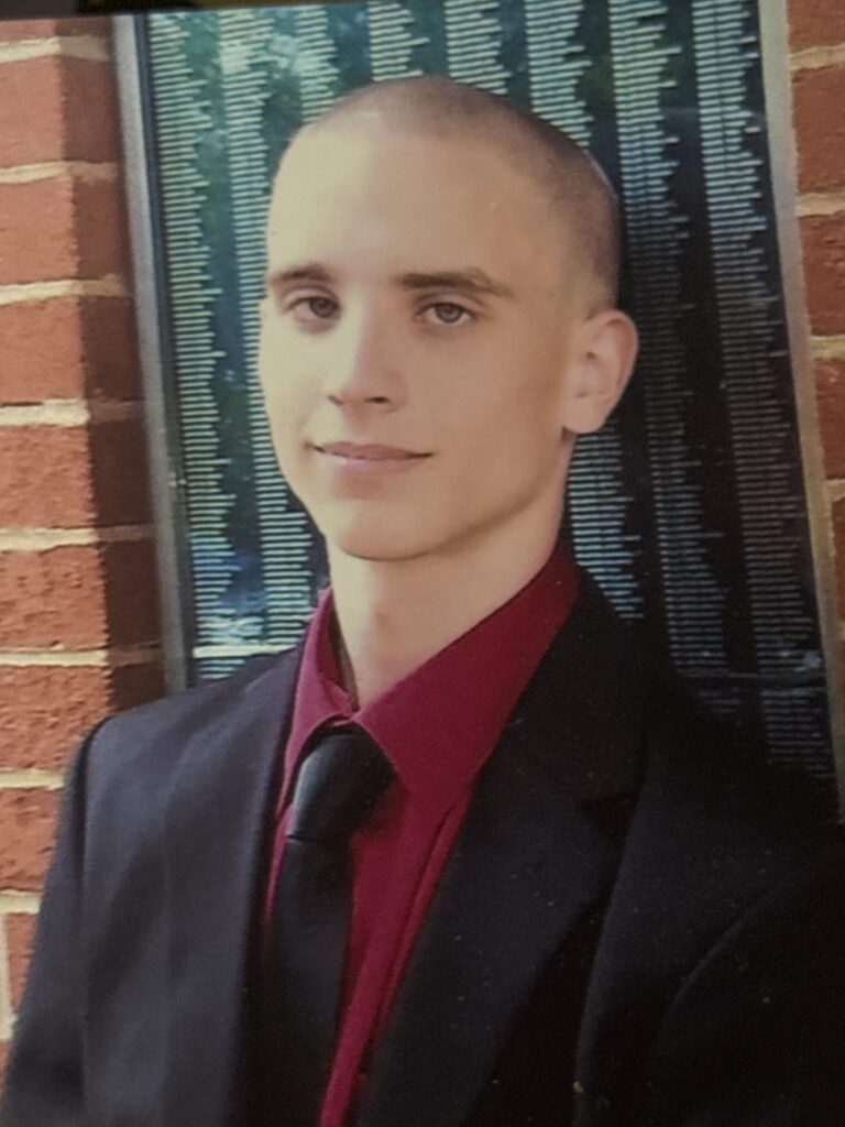 Young man in formal attire posing against a brick wall.