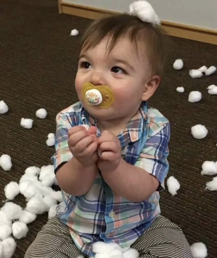 A toddler with a pacifier surrounded by white cotton balls.