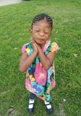 A little girl standing in the grass with her hands crossed.