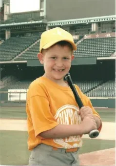 A young boy holding a baseball bat in front of an empty stadium.