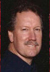 A man with a beard and mustache in front of red roses.