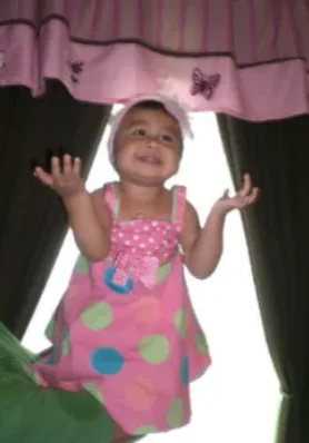 Fernanda (Fergy) Rodriguez A baby girl in pink dress standing under a canopy.