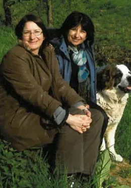 Two women and a dog sitting on the grass.