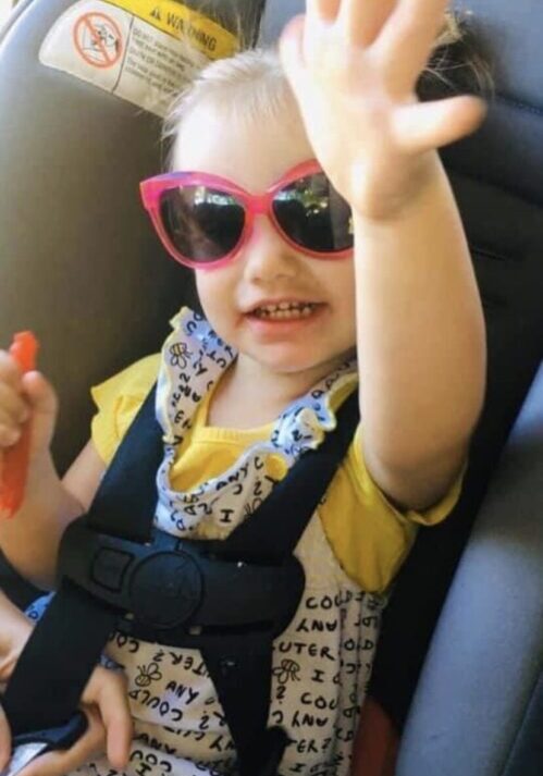 A little girl in a car seat wearing sunglasses.