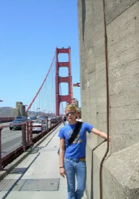 A man standing on the side of a road near a bridge.