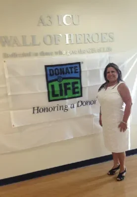 Maggie Rangel A woman standing in front of a wall of heroes sign.
