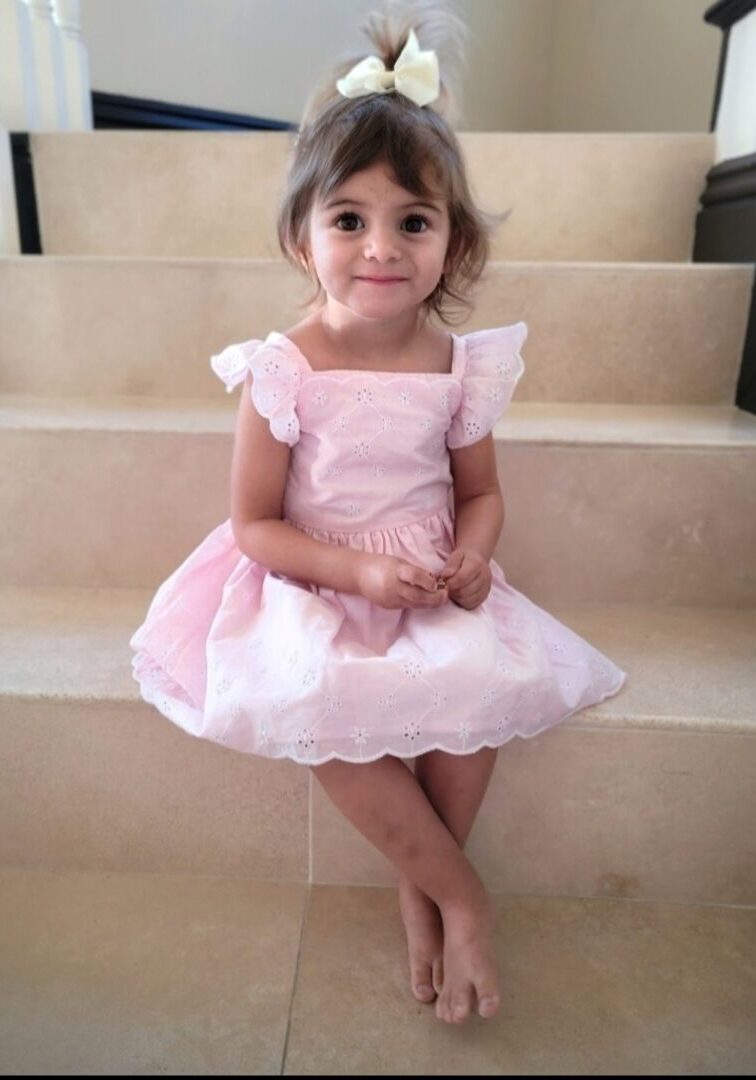 A little girl in pink dress sitting on steps.