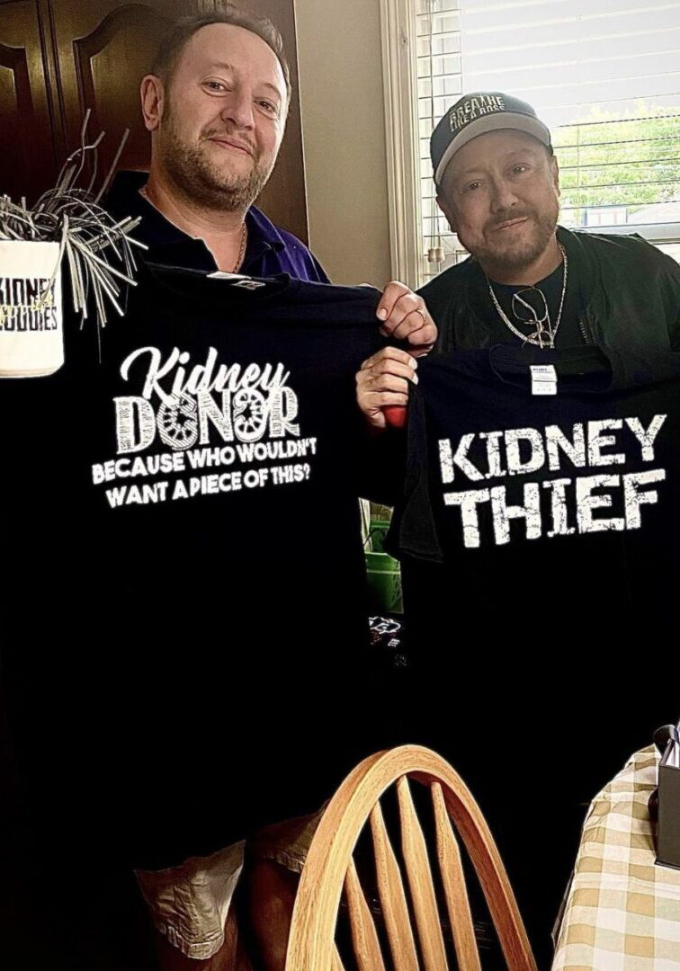 Two men holding up black shirts with the words kidney denial and kidney thief on them.