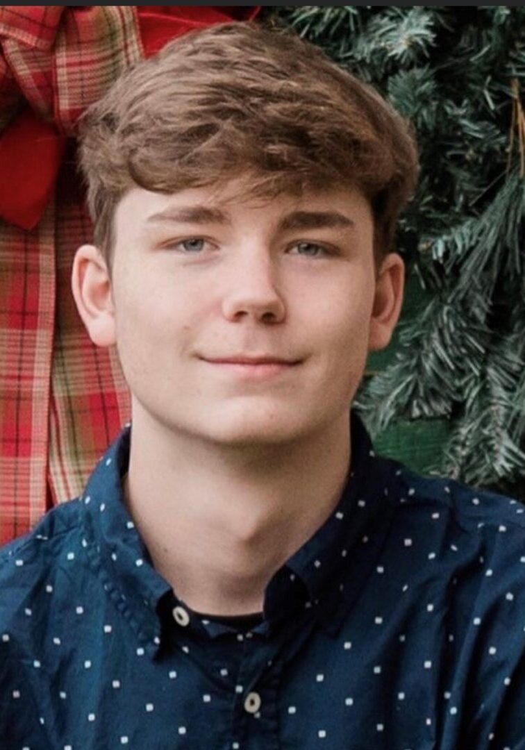 A young man in front of a christmas tree.