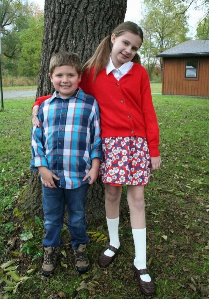 Two children standing next to a tree in the grass.