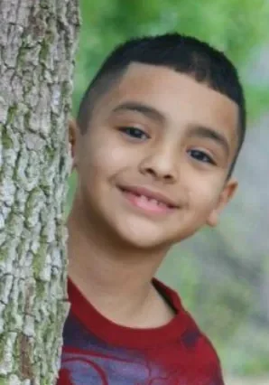 A young boy standing next to a tree.