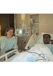 A woman sitting next to a man in a hospital bed.