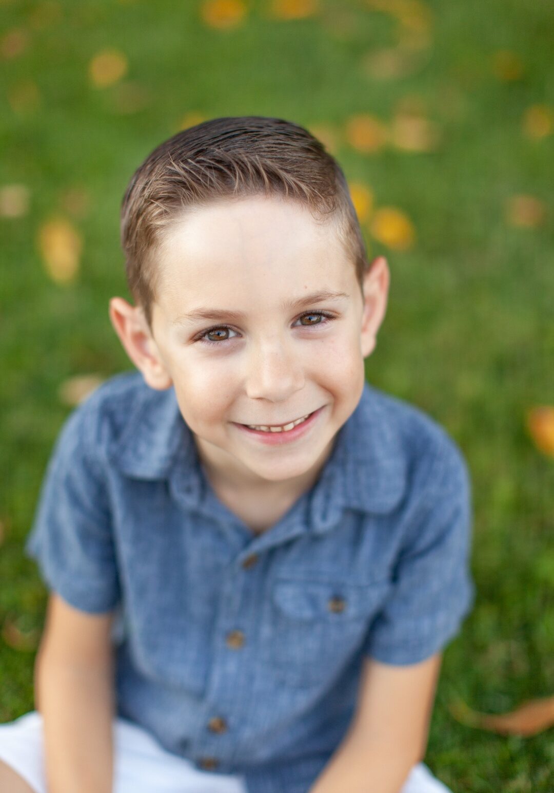 Screenshot_20230113_104523_Gallery A young boy sitting in the grass smiling for the camera.