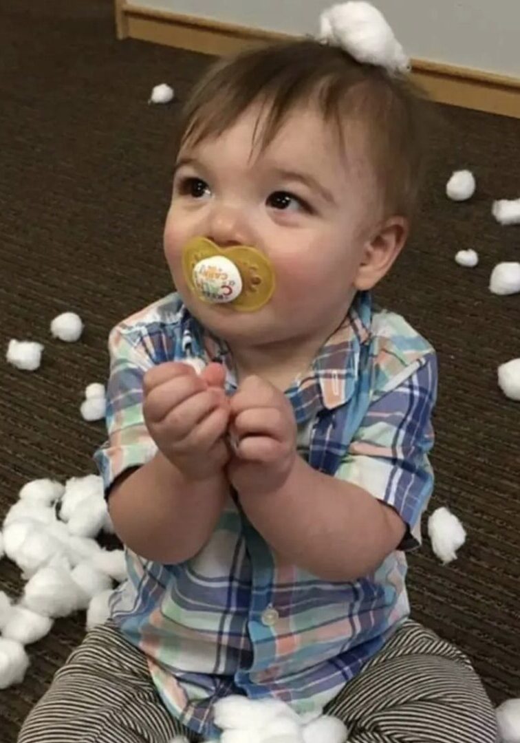 A toddler with a pacifier surrounded by white cotton balls.