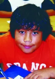 A young boy sitting at the table with his hands in his pockets.